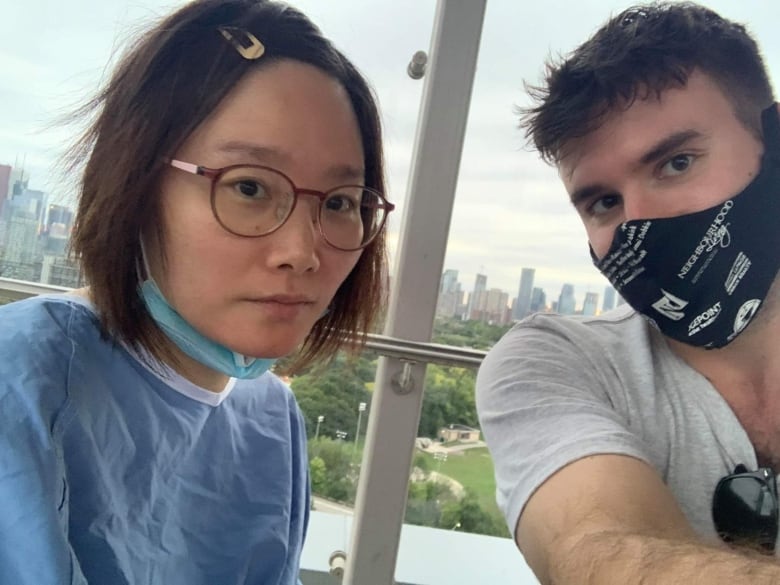 A woman wearing a hospital gown poses with a man wearing a face mask.