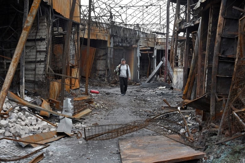A man walks through a burned out market building in Kharkiv, Ukraine, that is littered with rubble and twisted metal. 