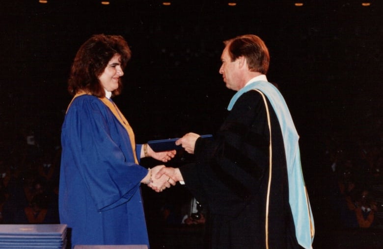A woman in graduation robe receives a diploma.