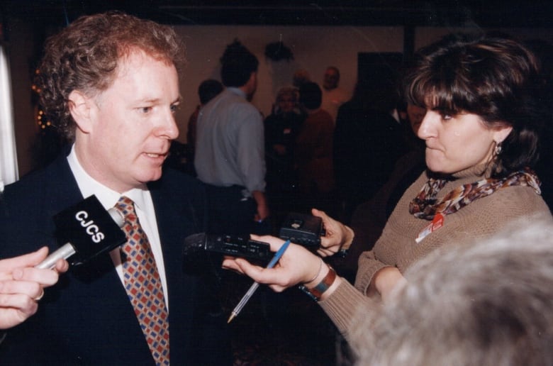 A reporter holds up a recorder to a curly-haired man.