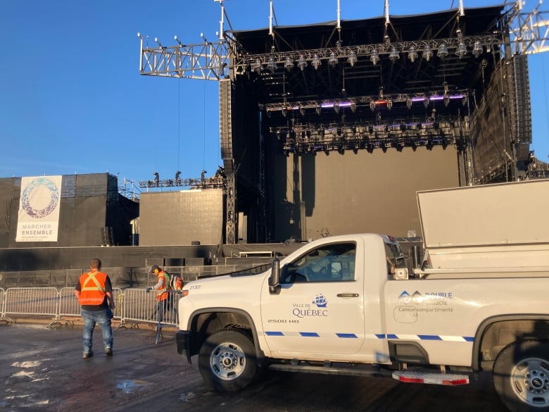Workers stand beside a white truck near a stage.