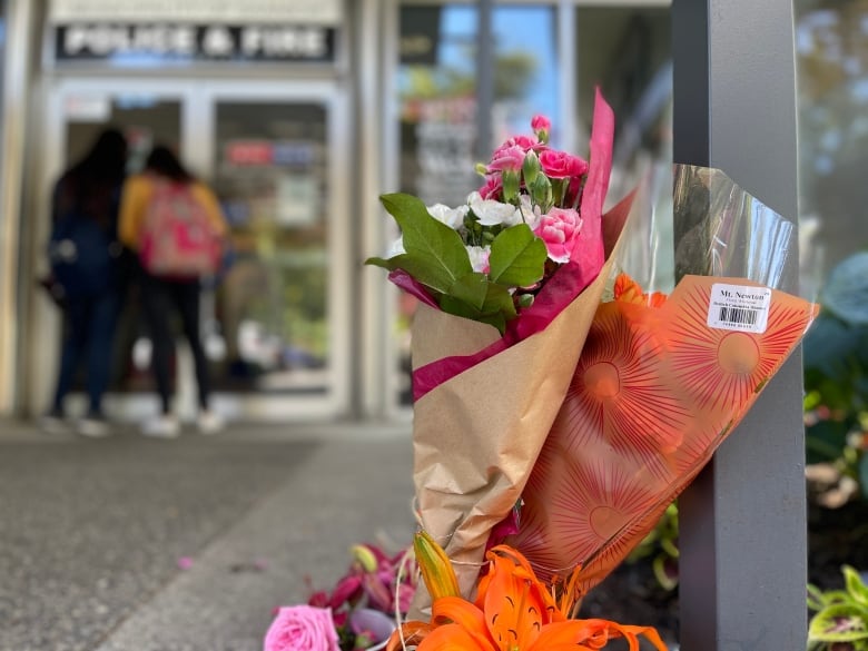 Members of the public look through the doors of Saanich, B.C.'s police department on Thursday, June 30, 2022, where bouquets of flowers have been placed in support of wounded officers — two days after a bank robbery ended with six officers wounded, two suspects dead, and locals reeling from the traumatic events.