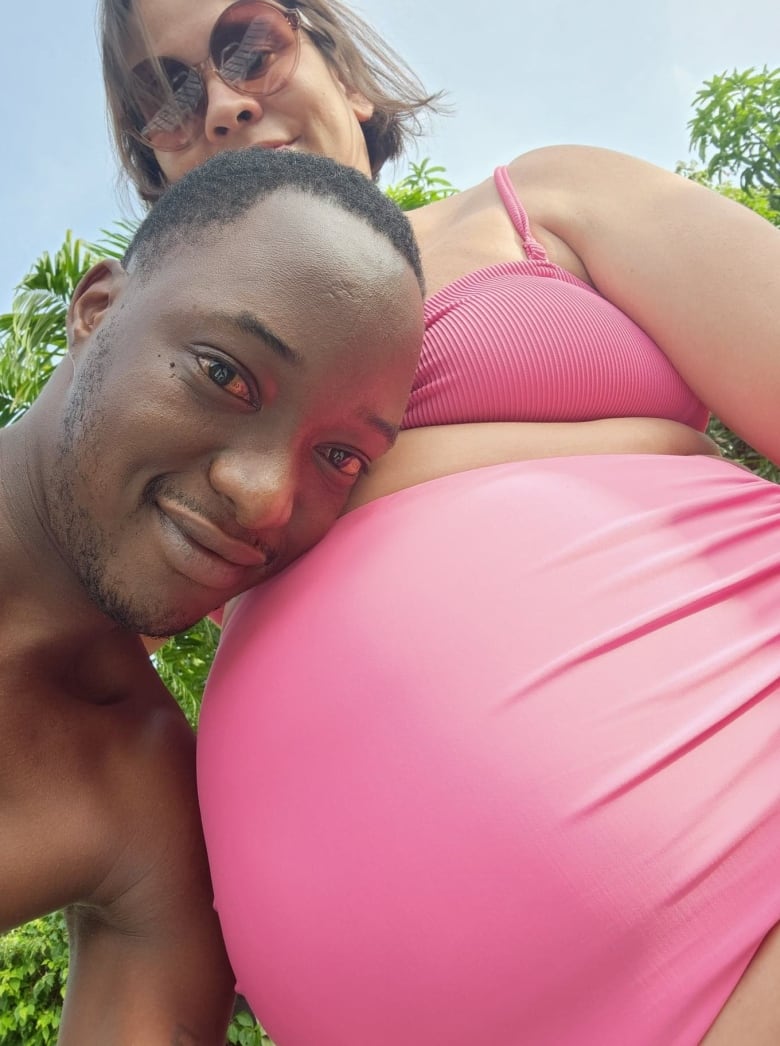 A pregnant woman in a pink bathing suit with her husband, smiling.