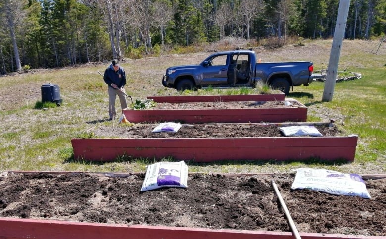 A man works on one of several raised gardening beds. 