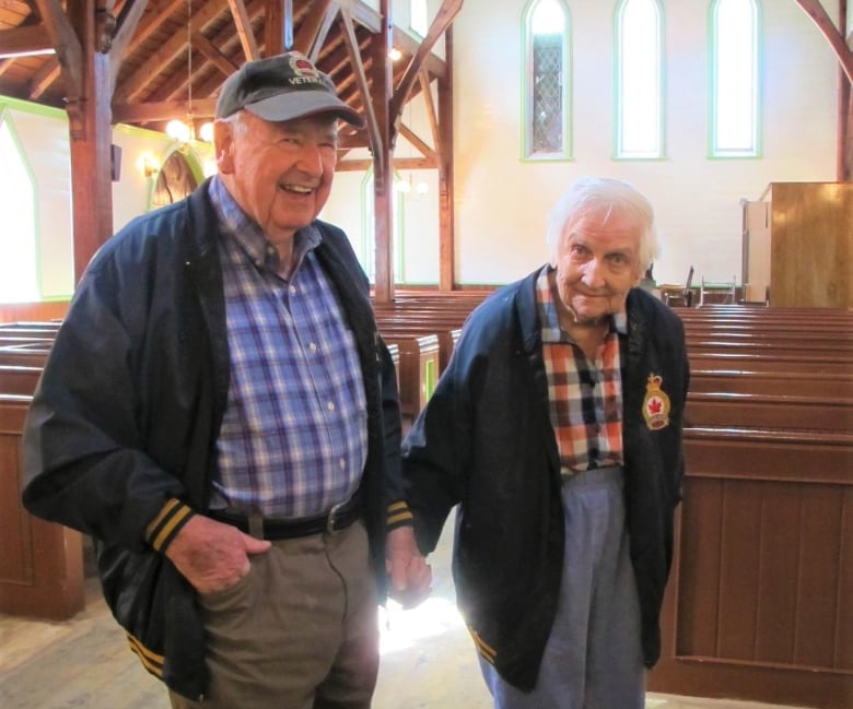 An elderly man and woman hold hands in a wooden church. 