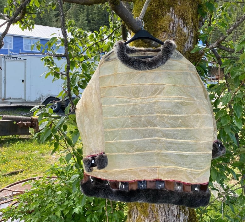 A translucent parka hangs from the branch of a tree.