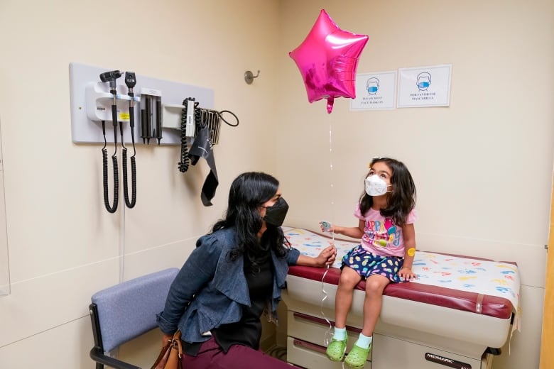 A mother and daughter sit in a doctor's office. The daughter is holding a balloon.