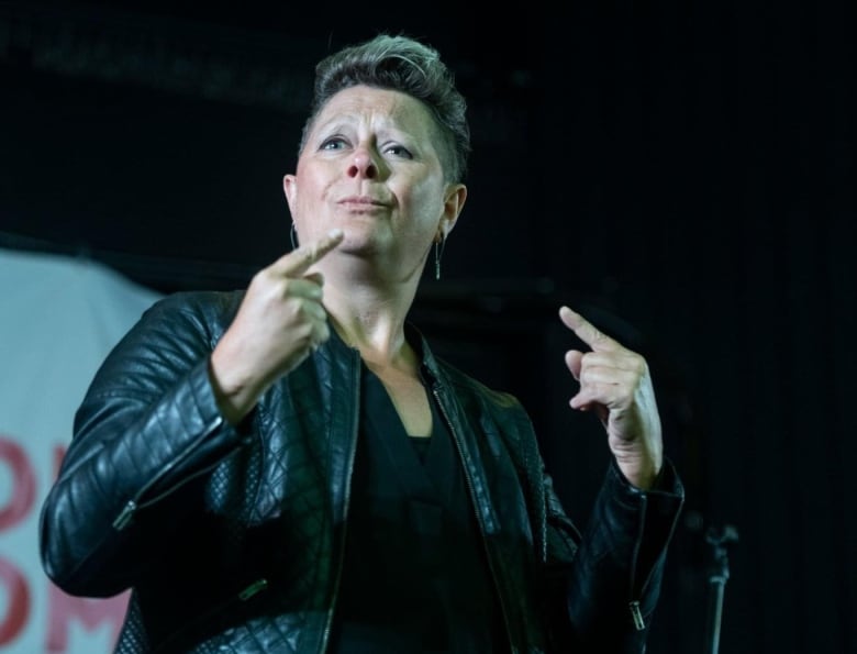 A woman stands on a music stage interpreting American Sign Language.