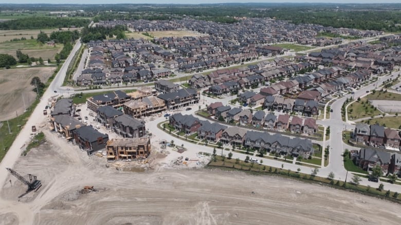 An aerial view shows rows of detached homes and an under-construction townhouse development. 
