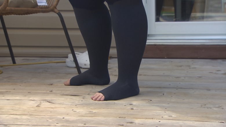 A woman stands on a deck with her toes poking out of a pair of stockings.