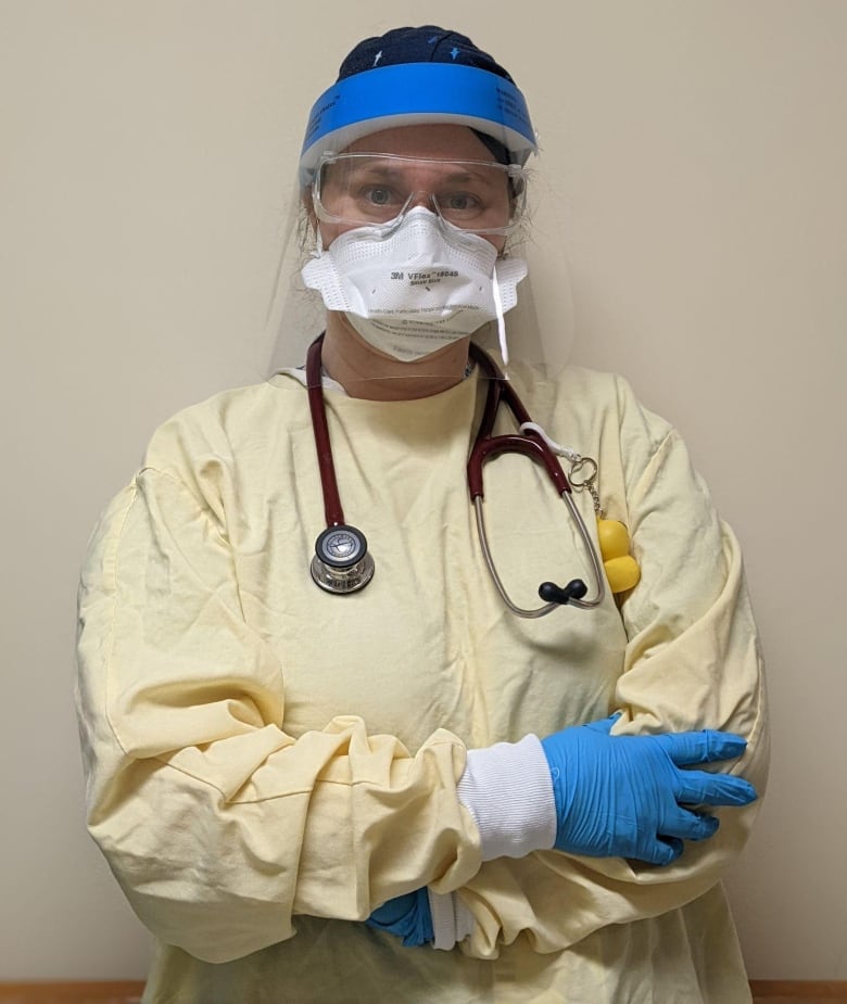 A woman with a stethoscope slung around a neck and wearing personal protective equipment, including a mask and face shield. 