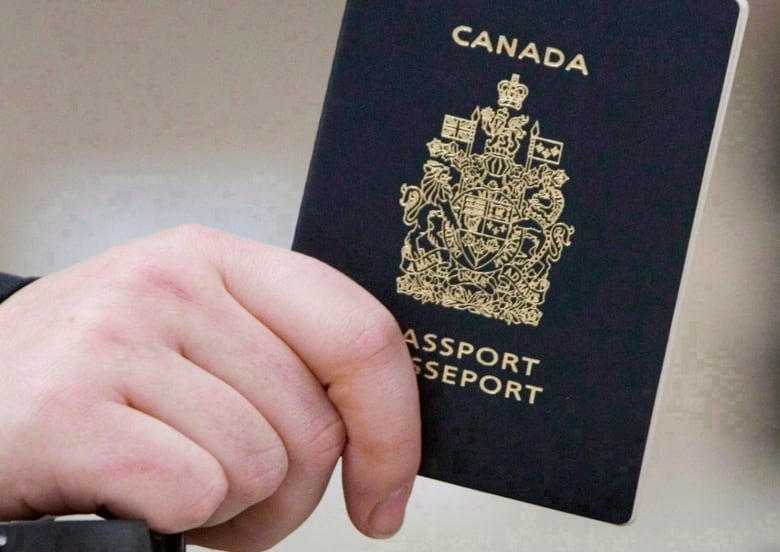A close-up photo shows a hand holding a Canadian passport. 