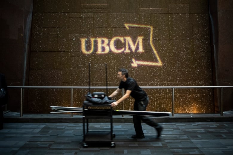 A man pushes a cart past a sign that reads 'UBCM'.