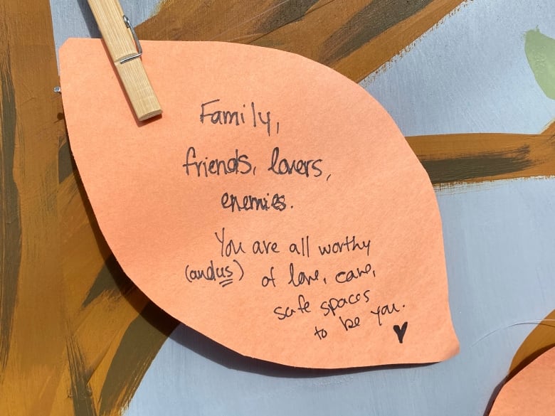 A piece of paper in the shape of a leaf, on which someone has written 'family, friends, lovers, enemies. You are all worth of love, care, safe spaces to be you.'