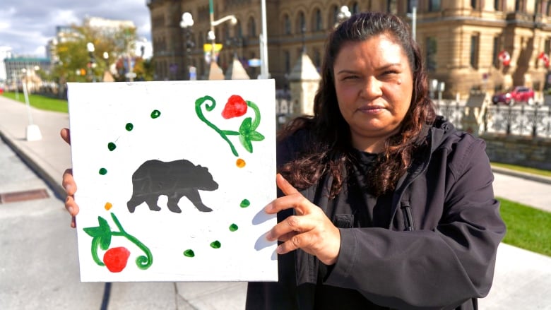 A woman holds up a painting of a bear and flowers.