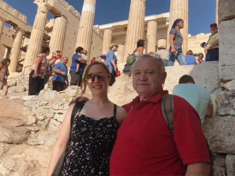 A man and a younger woman stand amid Greek ruins. 