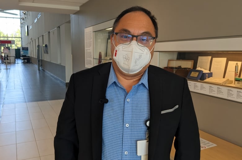 A doctor wearing a mask, blue shirt and dark blazer stands in the bright atrium of a medical research centre.