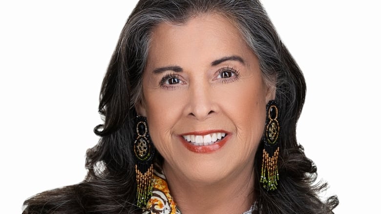 Close-up of a smiling individual with dark, shoulder-length hair, wearing colourful beaded earrings. 