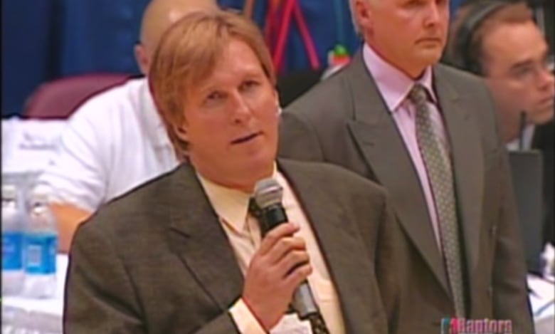 A man holding a microphone standing on a basketball court. 
