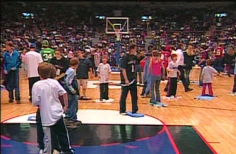 A crowd stands on a basketball floor with towels under their feet. 