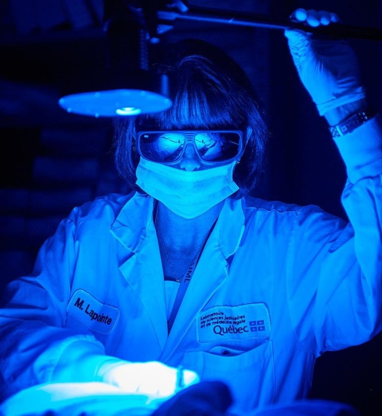 Woman in labcoat with sunglasses on under blue glow of light.