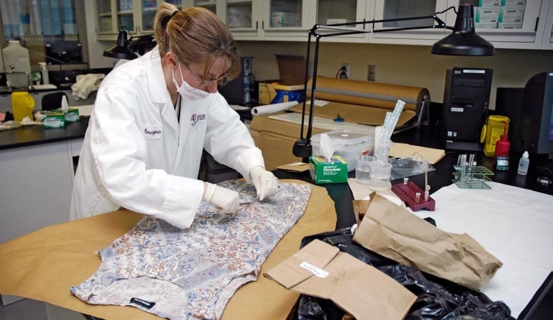 Woman in lab coat and gloves works on dress laid flat on table.