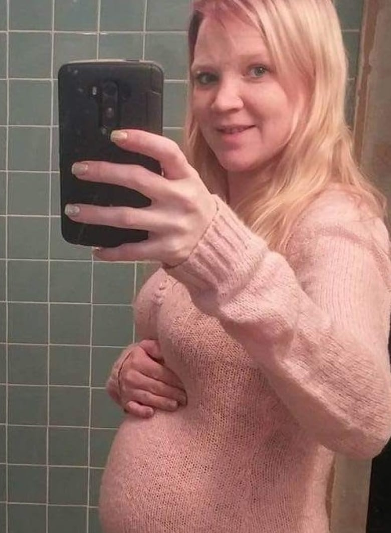A young blond woman uses a cellphone to take a photo of her pregnant form.