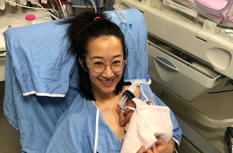 An Asian woman wearing a hospital gown holds her newborn baby. 