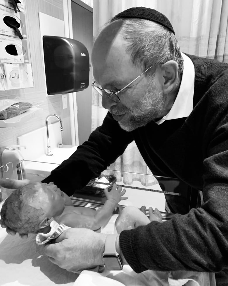 A man wearing a yarmulke holds a newborn baby in a hospital setting. 