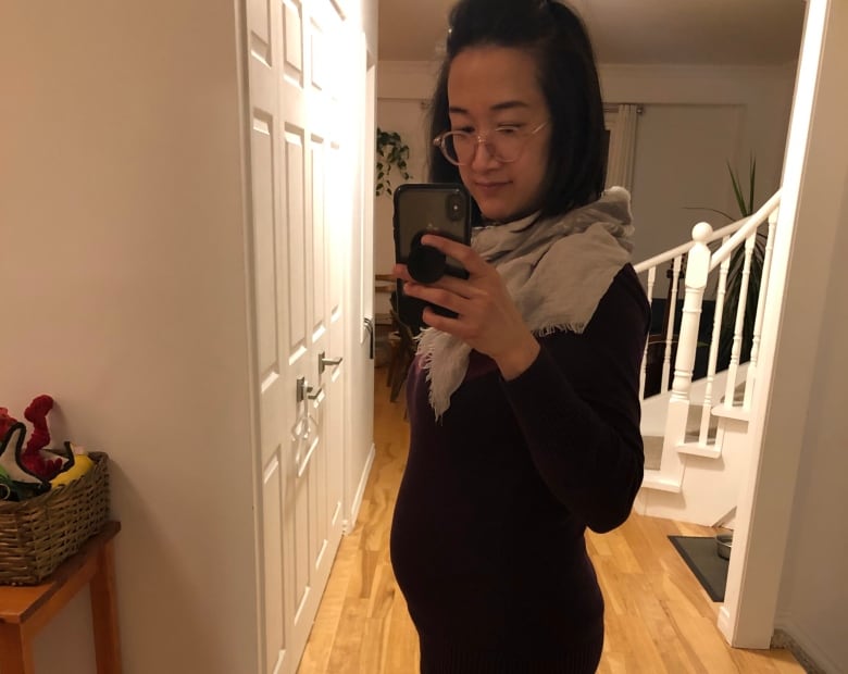An Asian woman holds a cellphone to take a photo of her pregnant belly. 