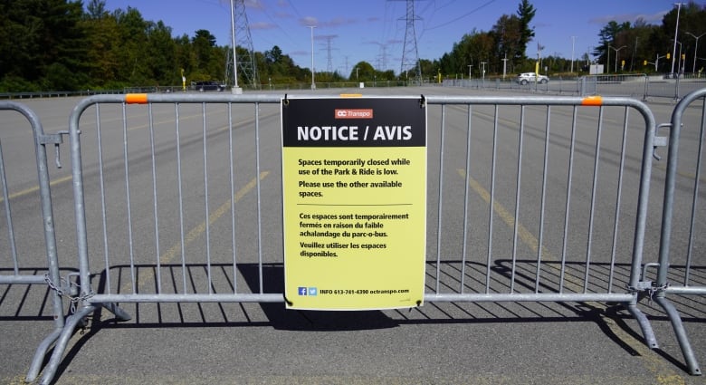 A yellow sign posted on a metal gate in an empty cement lot reads 'Spaces temporarily closed while use of the Park & Ride is low.'
