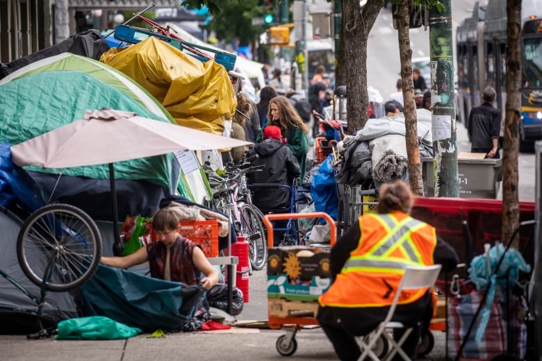 A group of people meet and talk near a row of tents on a sidewalk.