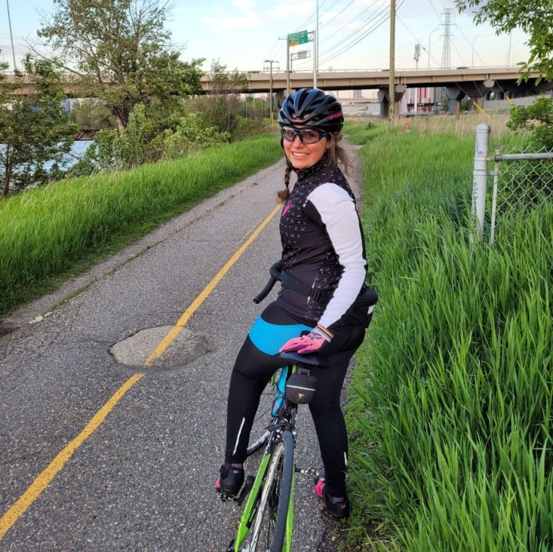 A woman looks back at the camera while standing with her bike.