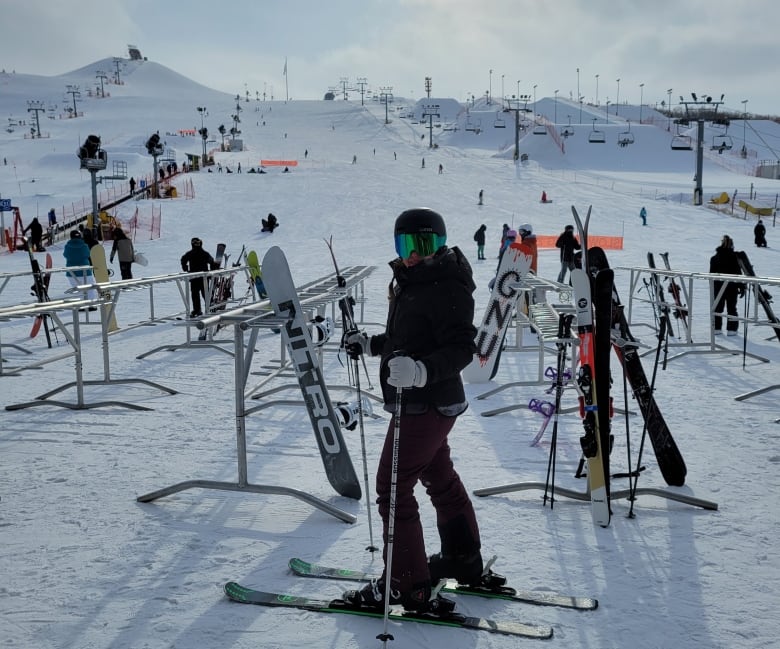 A woman on downhill skis stands at the bottom of a ski hill. 