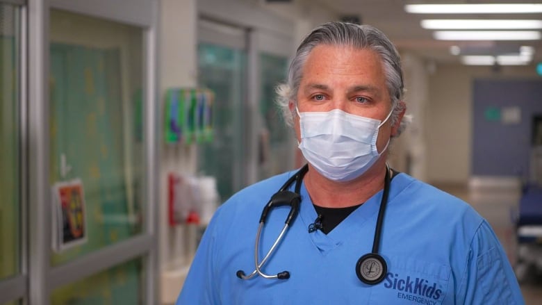 Grey-haired man in blue scrubs and a stethoscope around his neck.
