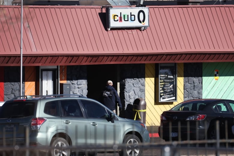 Cars parked in front of a single-storey, multicoloured building, with a sign on the roof that reads: "Club Q." Each letter is highlighted in a different colour, and the Q resembles a pierced ear with a hoop earring. 