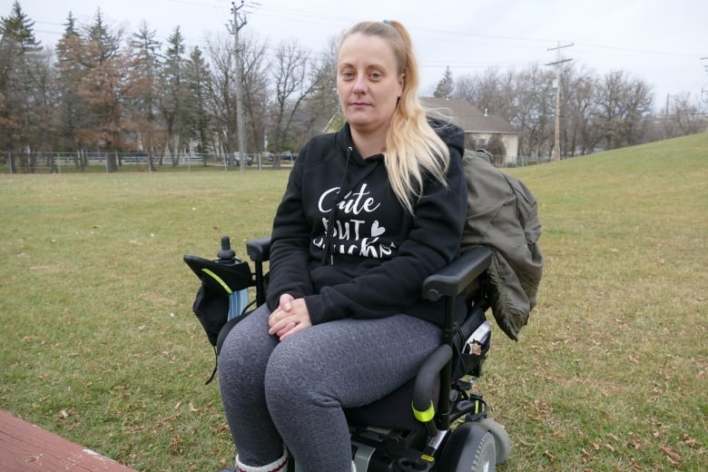 A woman in a wheelchair with long blonde hair in a ponytail and a black sweatshirt.