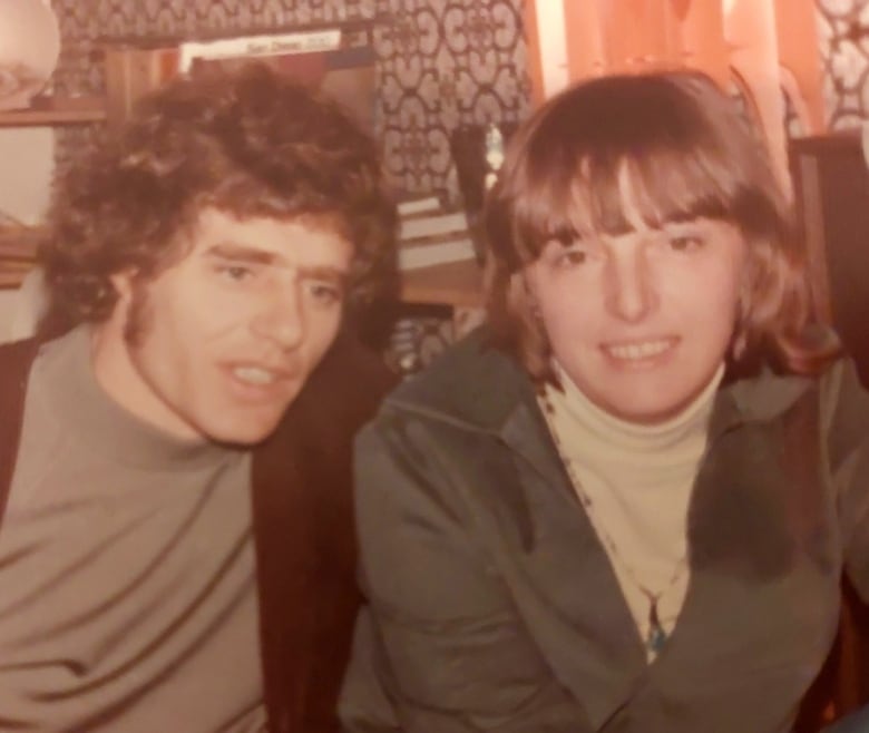 A young man, left, and woman, sit close together and smile. The photo is slightly faded, showing that it was taken decades ago.