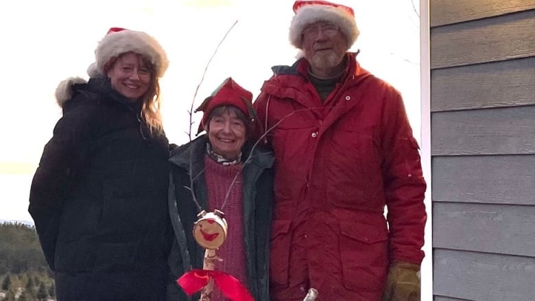 A couple with their grown daughter, all three smiling and wearing Santa hats. 