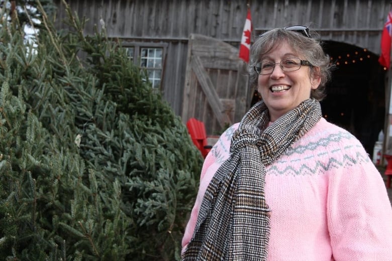 Individual in a pink sweater and scarf smiling broadly beside a Christmas tree.