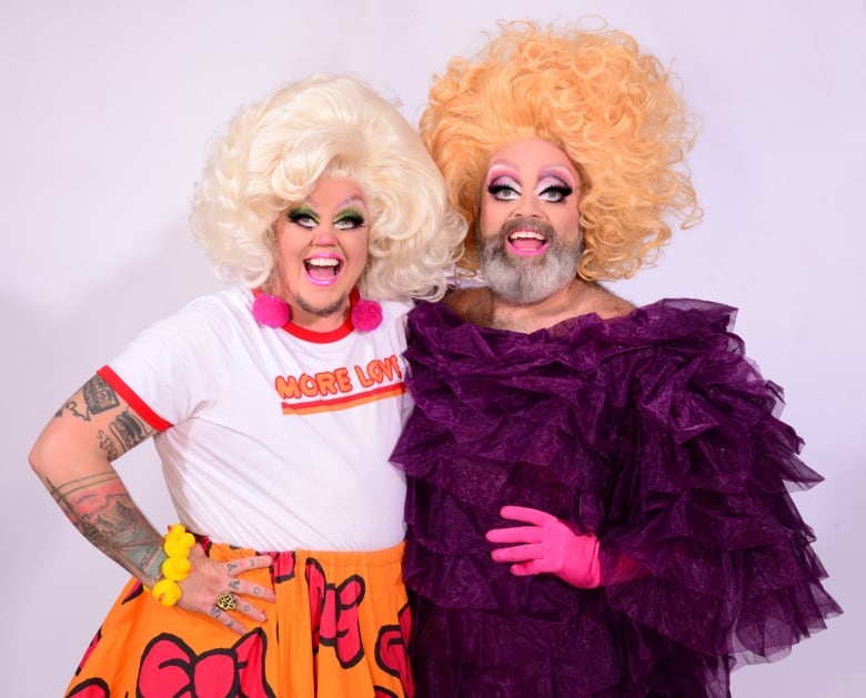 Deux artistes drag de Toronto sont assis ensemble dans des tenues lumineuses avec de grands sourires 