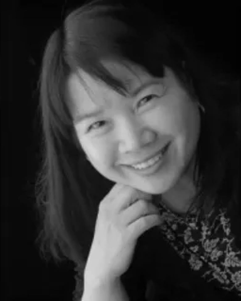 Une photo en noir et blanc montre une femme d'Asie de l'Est aux cheveux mi-longs, posant la tête inclinée sur le côté et la main sous le menton.