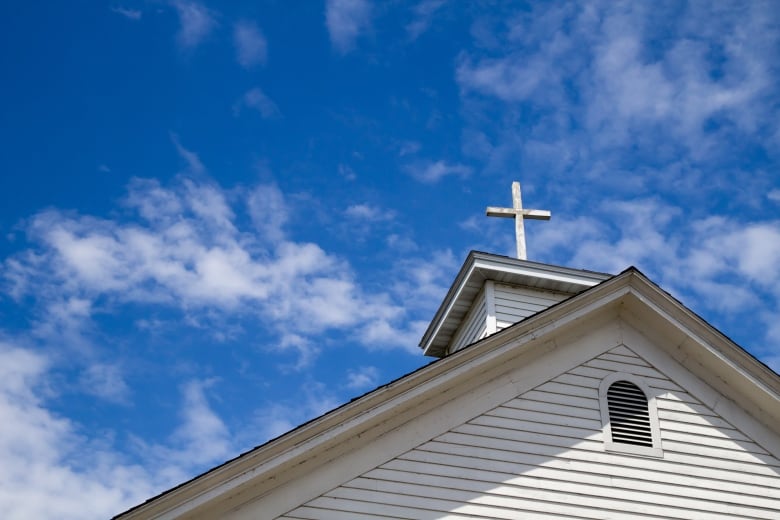 A cross is perched on the roof of a white church building. 