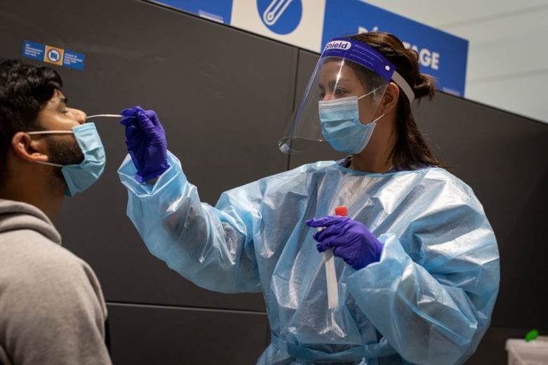 A woman wearing a mask, gloves and other protective gear carries out a nose swab on a man.