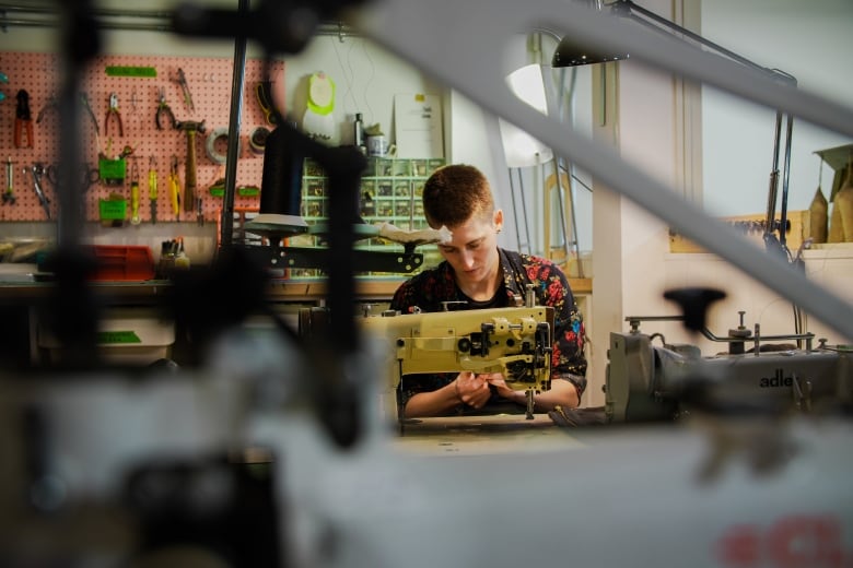 A person in a workshop sits behind a sewing machine, repairing a garment.