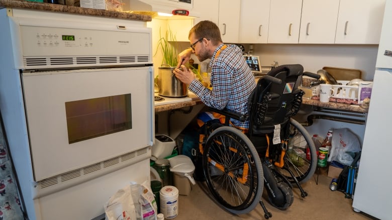 Un homme en fauteuil roulant cuisine dans une cuisine.