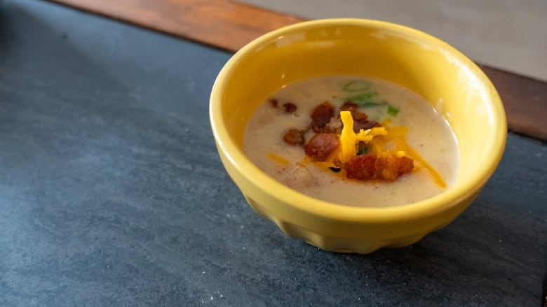 A bowl of creamy white soup topped with bacon bits and green onions.