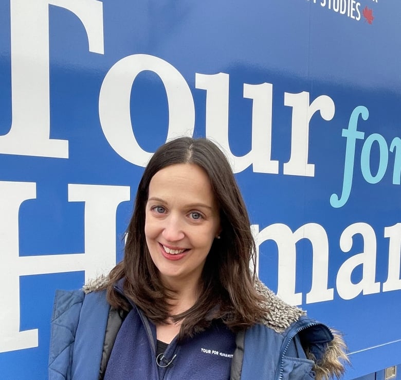 A woman stands beside a bus with 'Tour for Humanity' painted on its side.