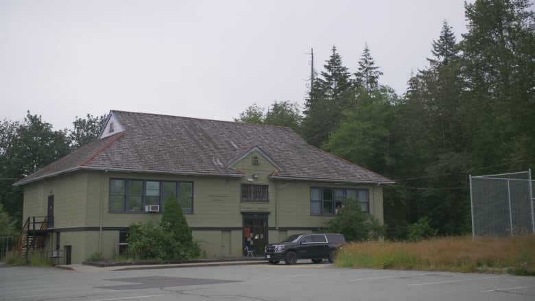 A green building stands in amongst trees. There is a black vehicle parked out front.