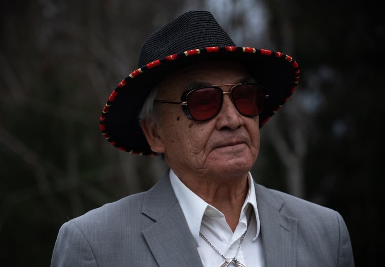 A man wearing a hat, sunglasses and a suit jacket stares off into the distance